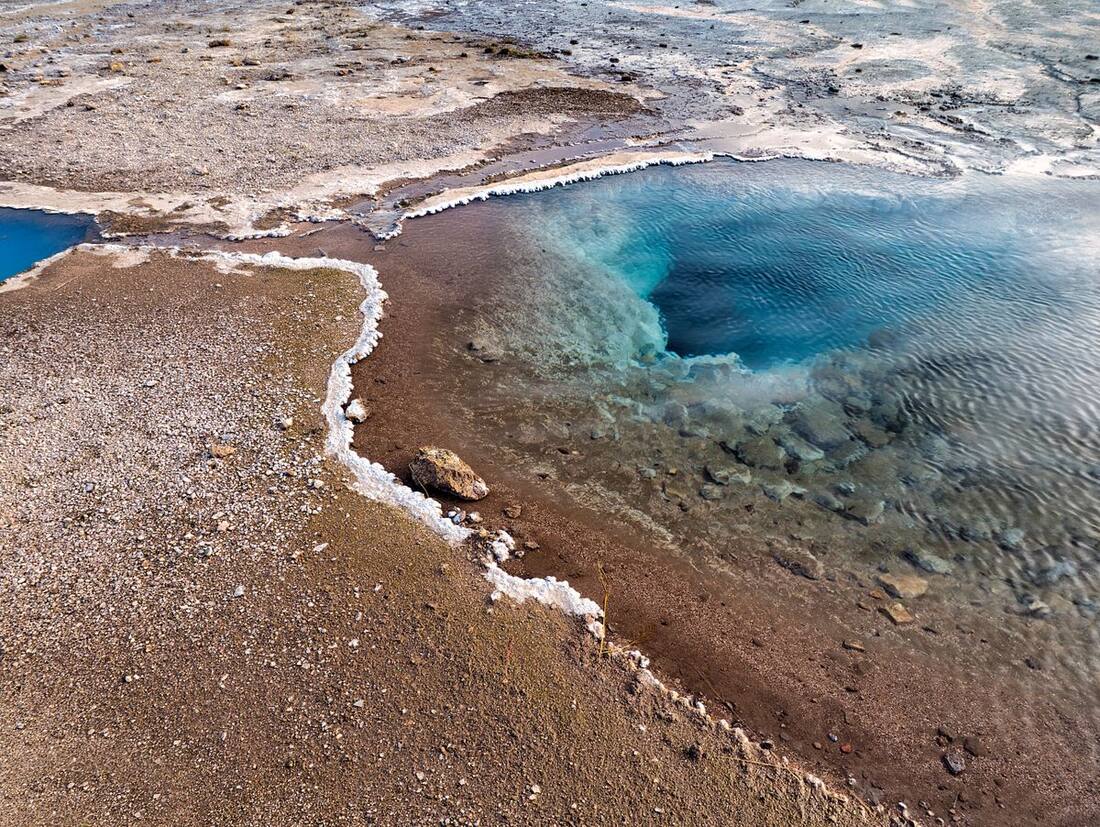 Aerial view of a vivid blue geothermal pool surrounded by mineral-encrusted volcanic terrain, Iceland