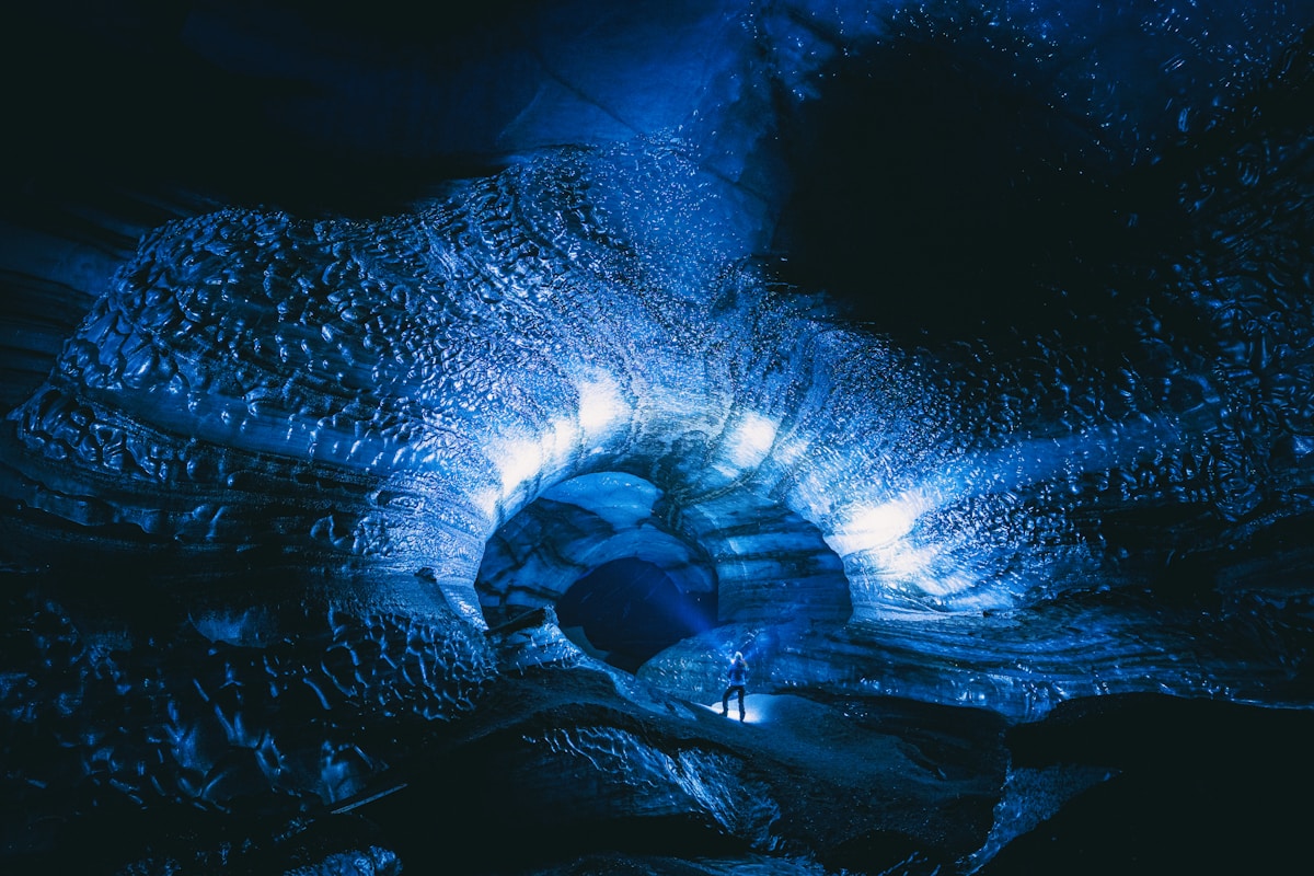 Person standing inside a glowing blue ice cave at Katla glacier, Iceland