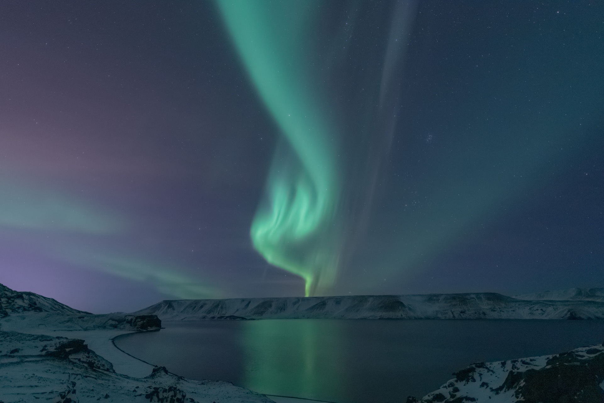 Vivid green and purple aurora borealis reflected over a snowy Icelandic fjord landscape at night