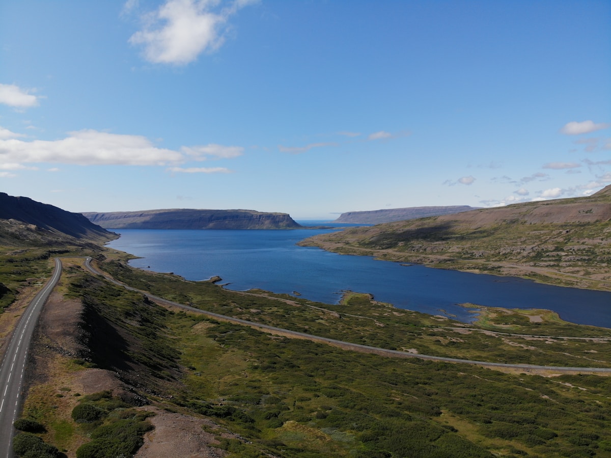 A Westfjords fjord road with flat-topped cliffs and blue water, Iceland