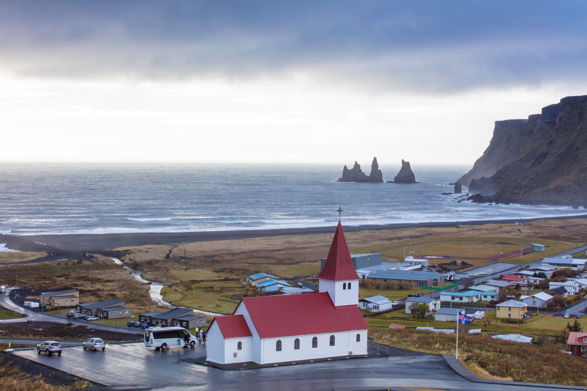 Vík village with red-roofed church, Reynisdrangar sea stacks and black sand coast, south Iceland