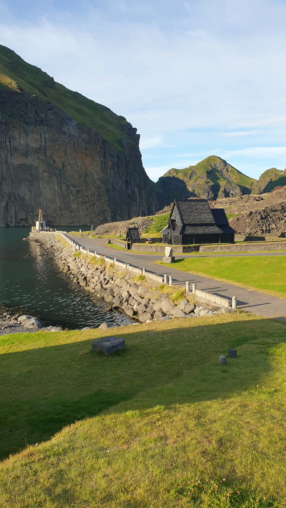 The historic stone harbour breakwater at Heimaey with green volcanic cliffs, Vestmannaeyjar, Iceland