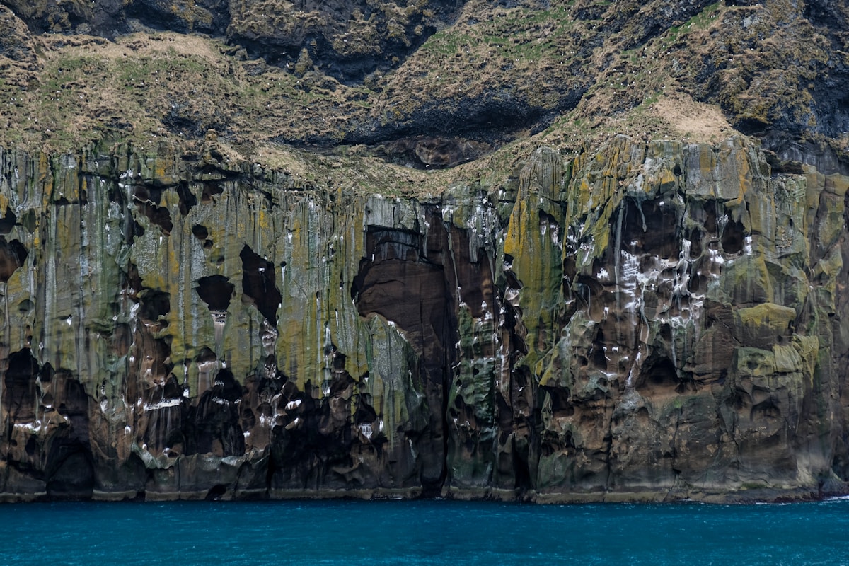 Brown and green volcanic rock formation rising from the blue sea at Vestmannaeyjar, Iceland