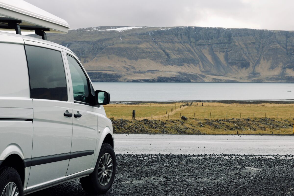White campervan parked on an Icelandic coastal road with fjord and dramatic mountains behind