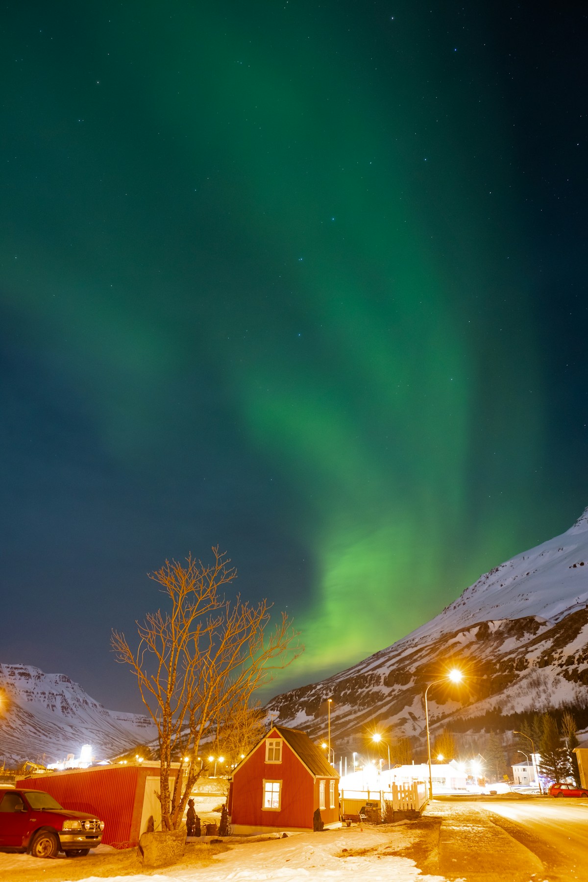 Aurora borealis over red house and snow-covered mountains, Seyðisfjörður, Iceland