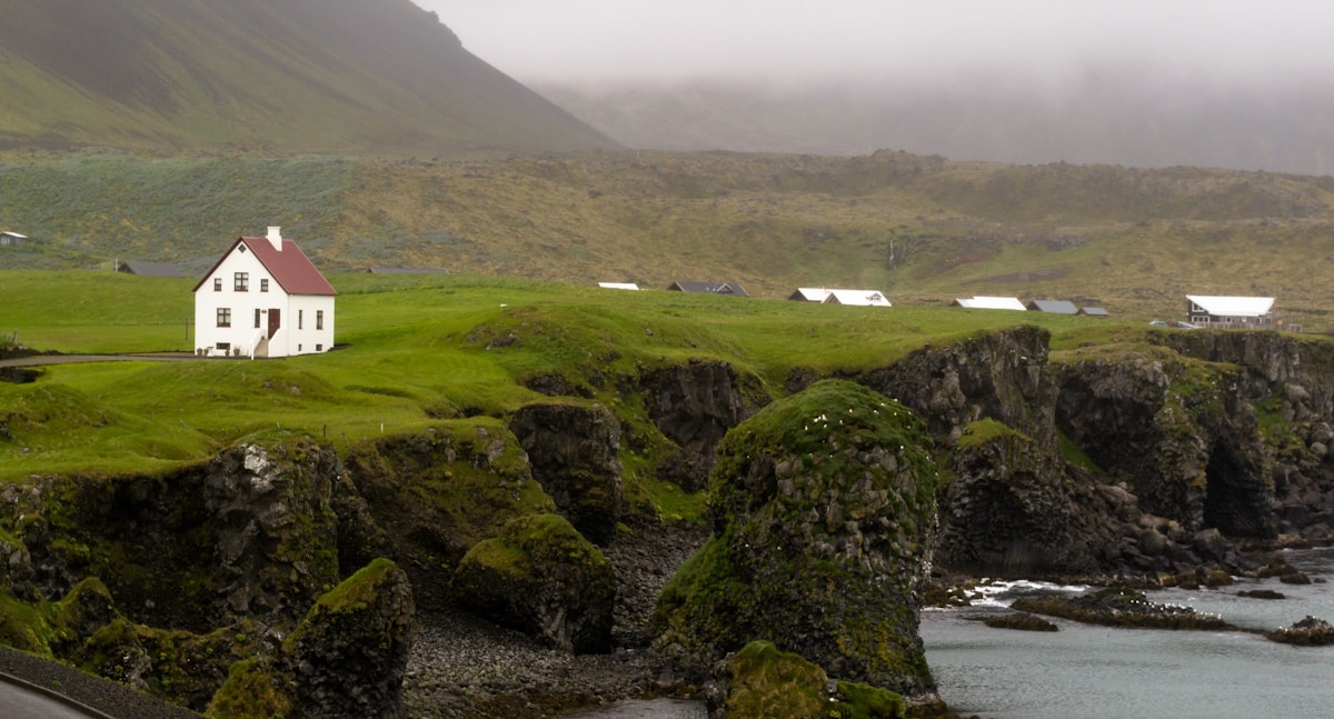 White farmhouse on green coastal lava cliffs with misty mountains, Snæfellsnes peninsula, Iceland