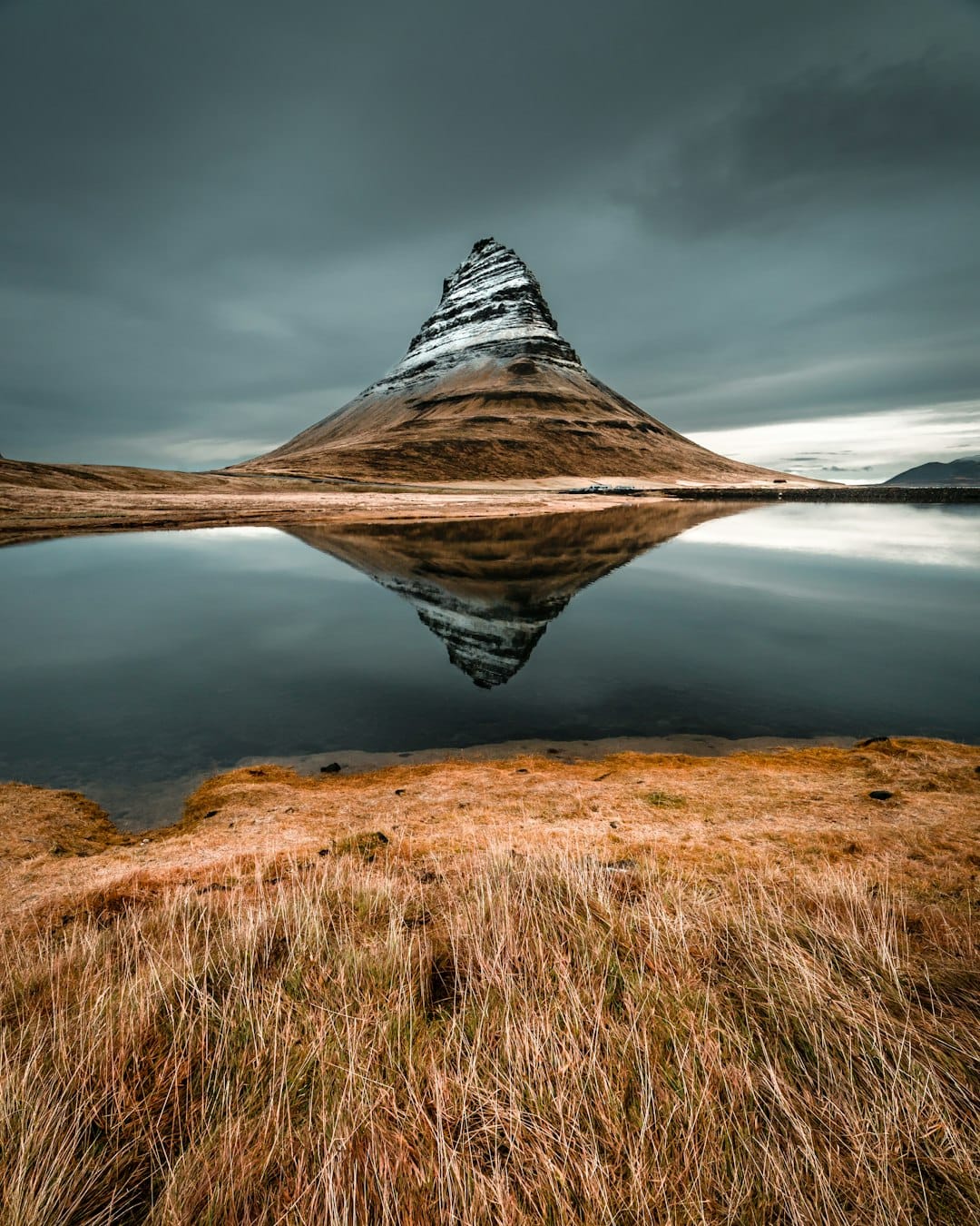 Kirkjufell mountain reflected in a still lake under a dramatic grey sky, Snaefellsnes Peninsula, Iceland