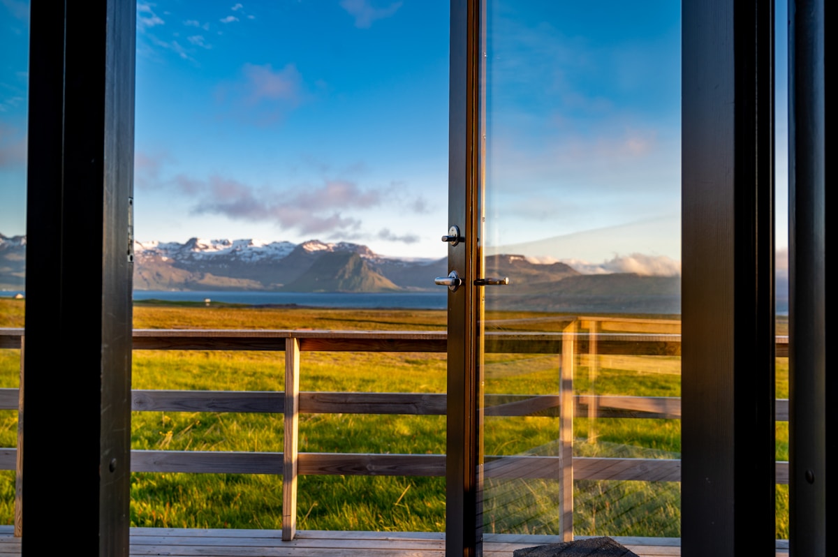 Open door from a cottage deck revealing a green field and snow-capped mountains, DÍS Cottages, Grundarfjörður, Iceland