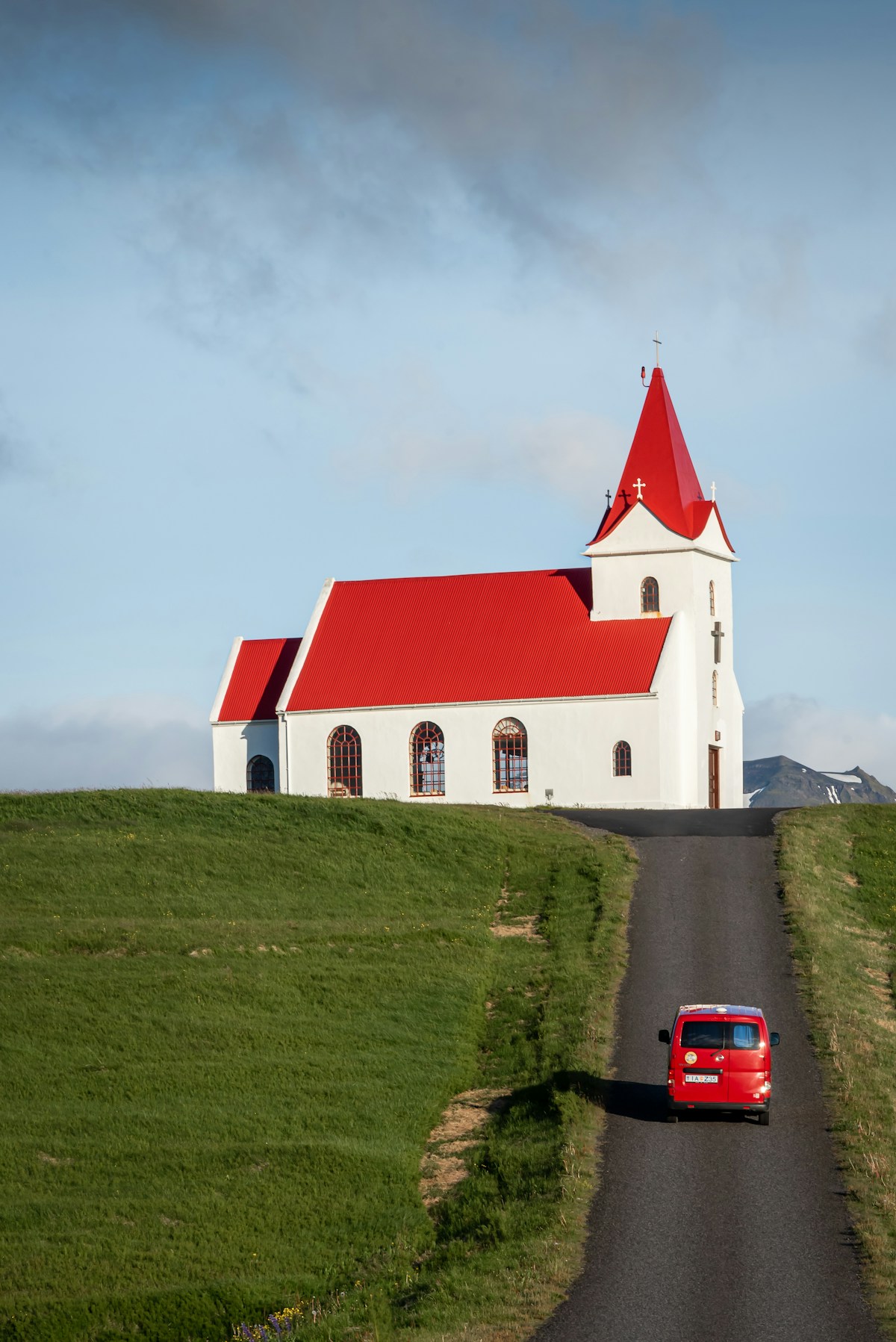 Red car driving down a road next to a white church in Iceland