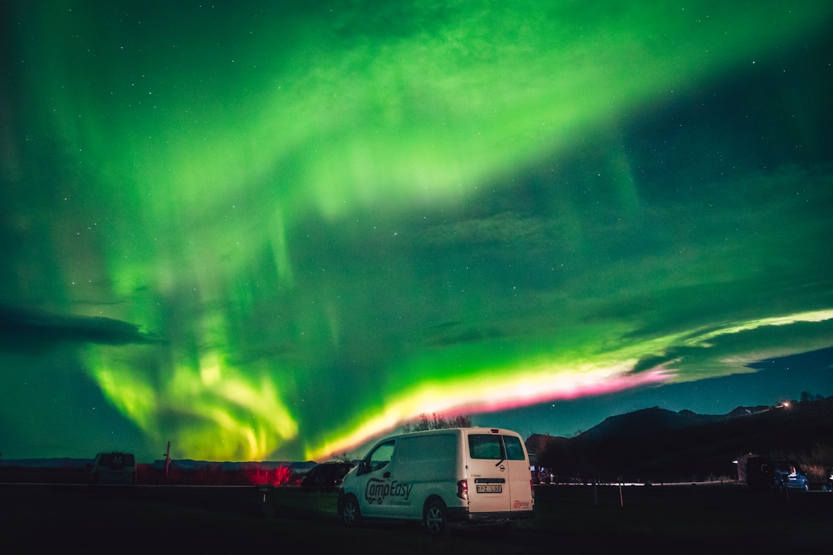 Rental campervan parked beneath green northern lights in Iceland