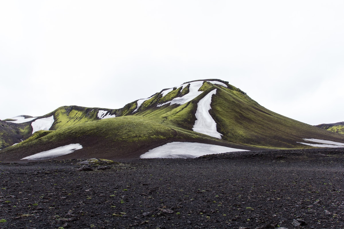 Green moss-covered mountain with patches of snow under white sky, Iceland highland landscape