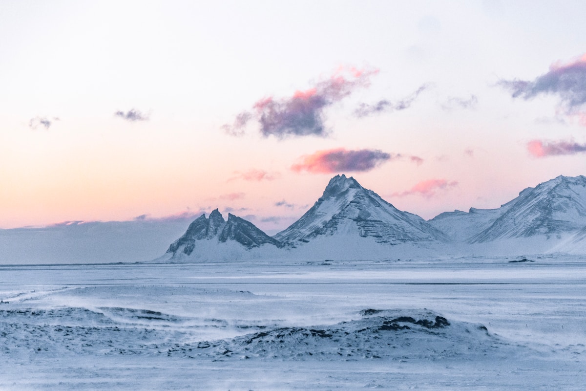 Snow-covered jagged mountain peaks under a pink and purple winter sky, Iceland