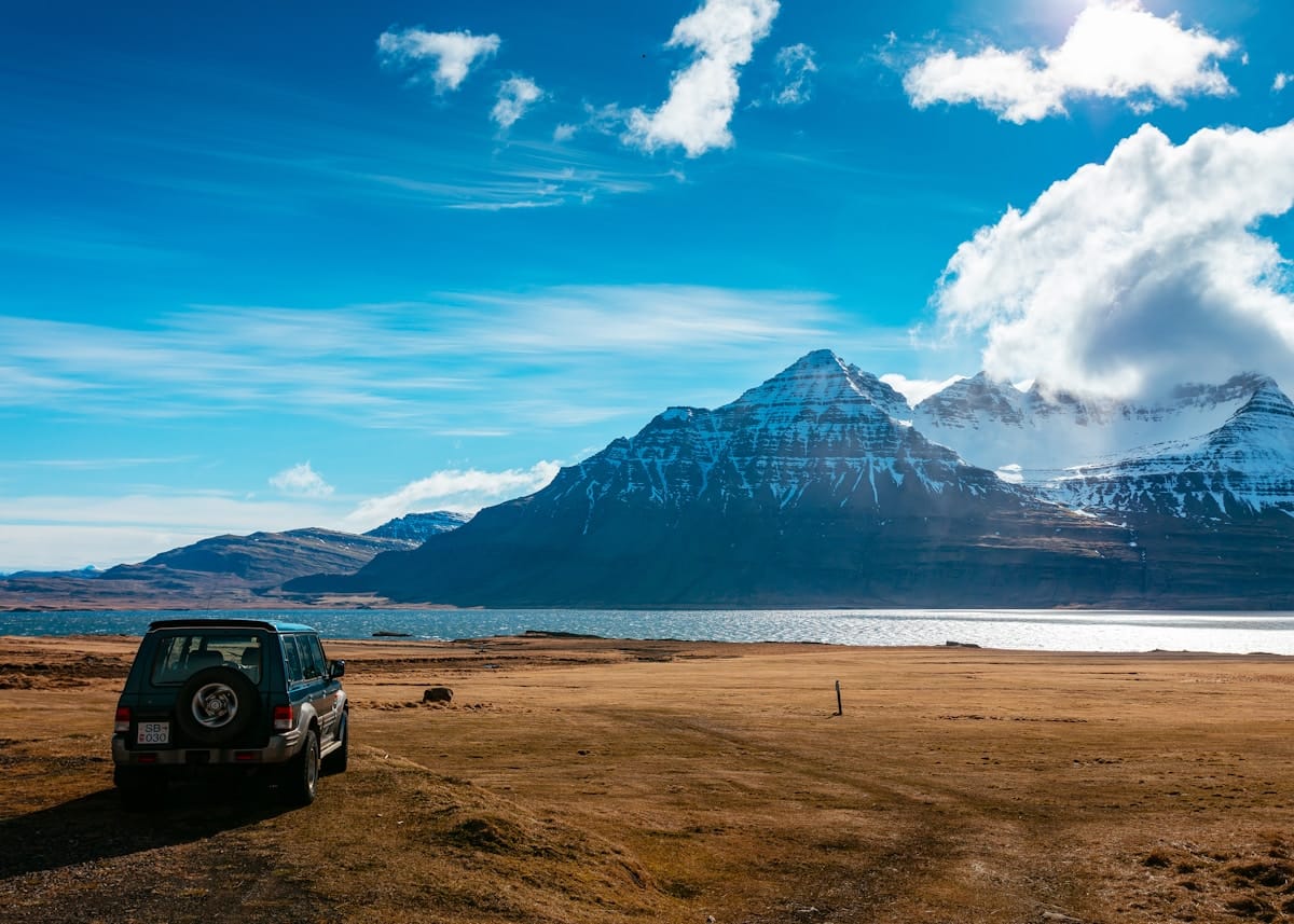 4WD SUV parked on a brown volcanic field in front of a fjord and snow-capped mountains, Iceland