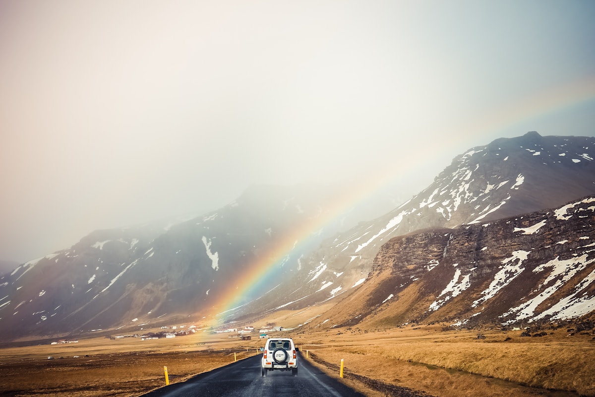 White rental car driving past mountains on the Icelandic Ring Road under a rainbow