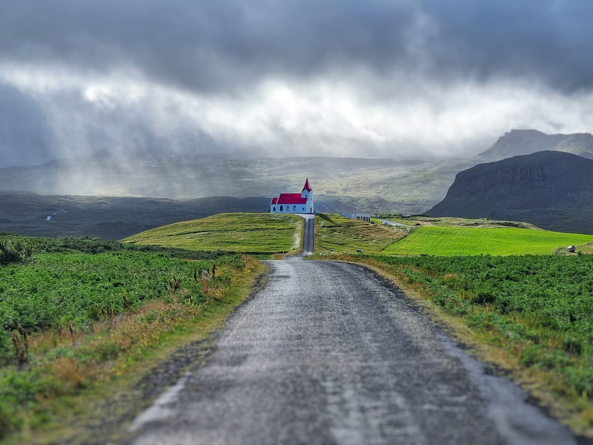 Road leading to a white church with red roof on Snæfellsnes hillside under dramatic storm clouds, Iceland