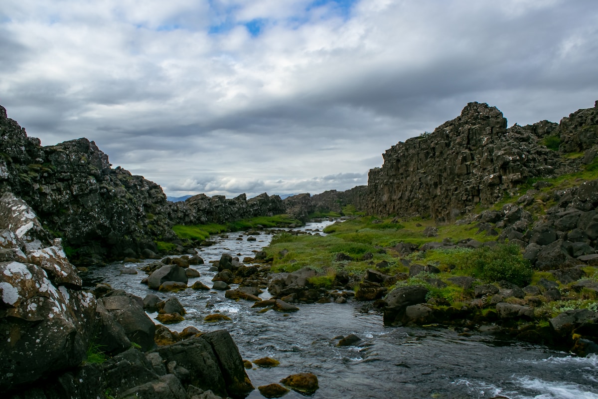 Green and brown rocky mountain beside river under blue sky, Iceland — travel insurance