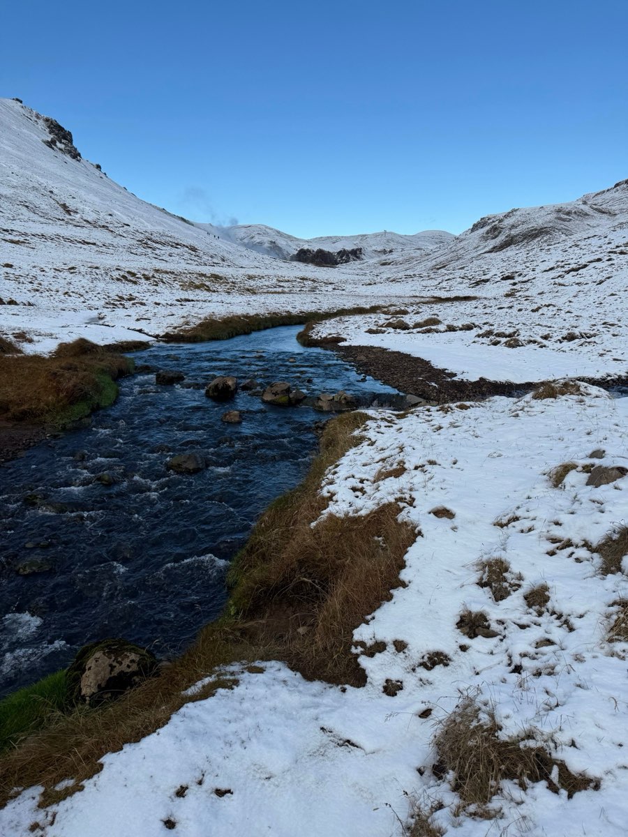 Snowy Iceland highland winter landscape with a clear blue river winding through white hills under blue sky