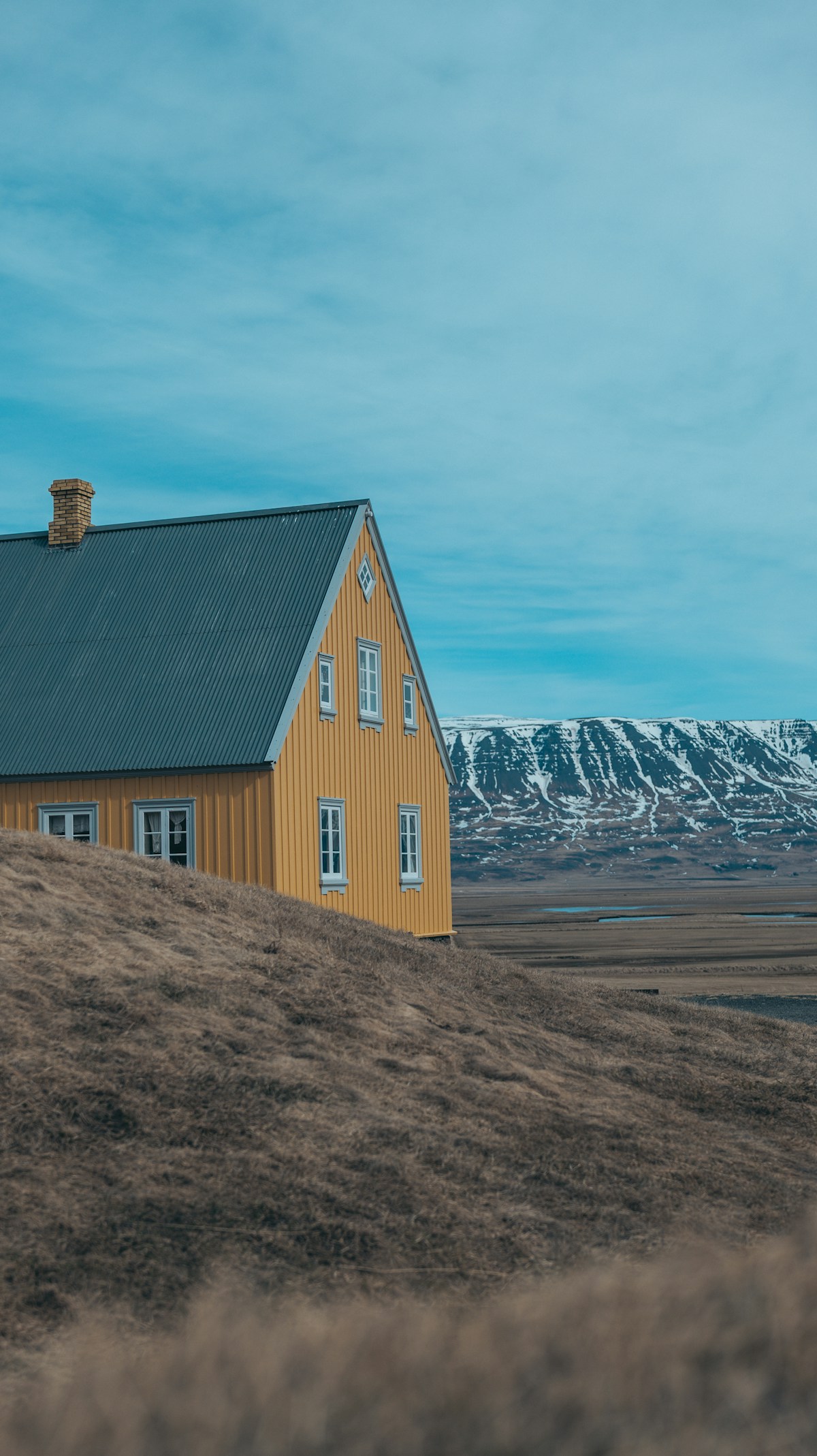 Yellow house on a grassy hill with snowy mountains in the background, Iceland