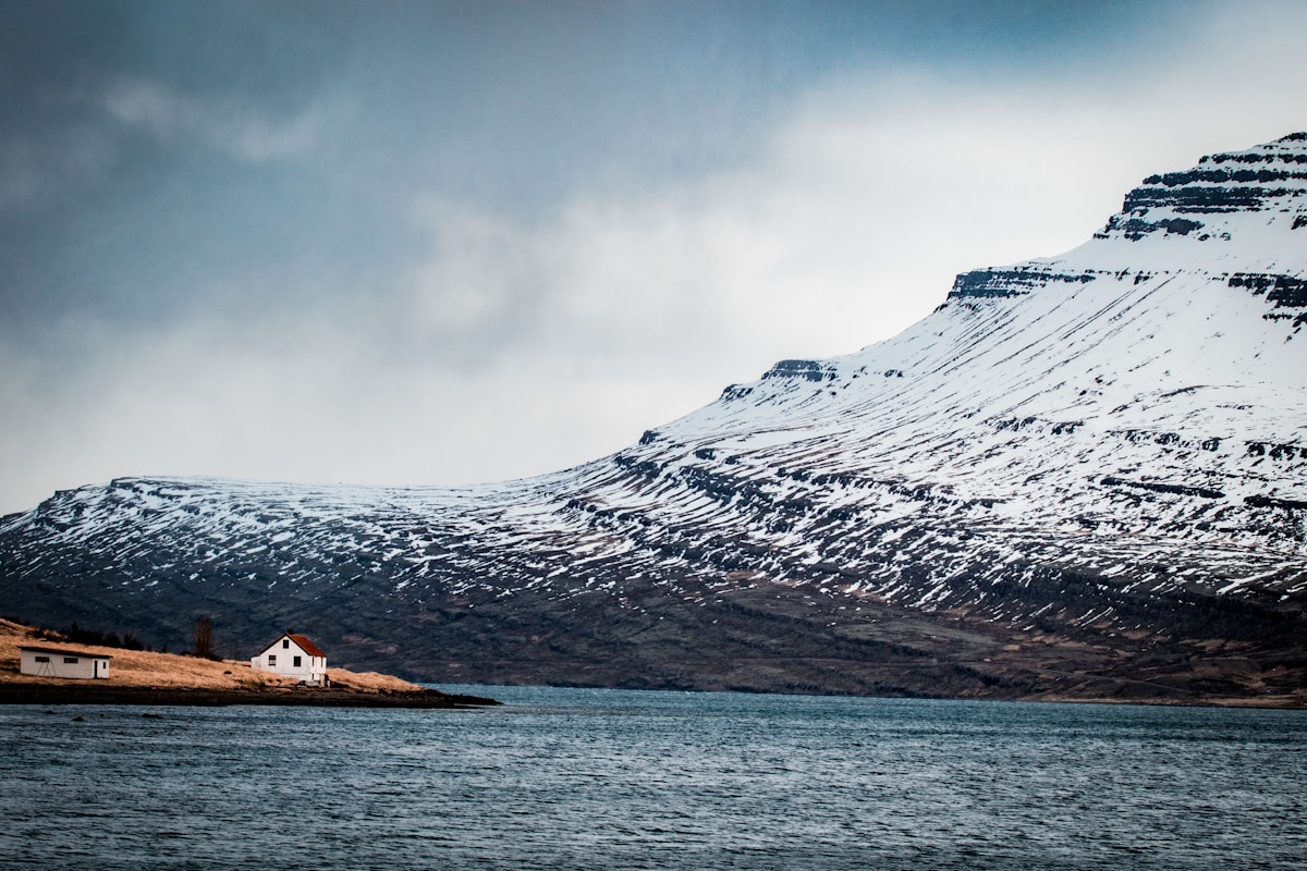 Lone farmhouse beside a fjord with dramatic snow-capped mountains at Reyðarfjörður, East Iceland
