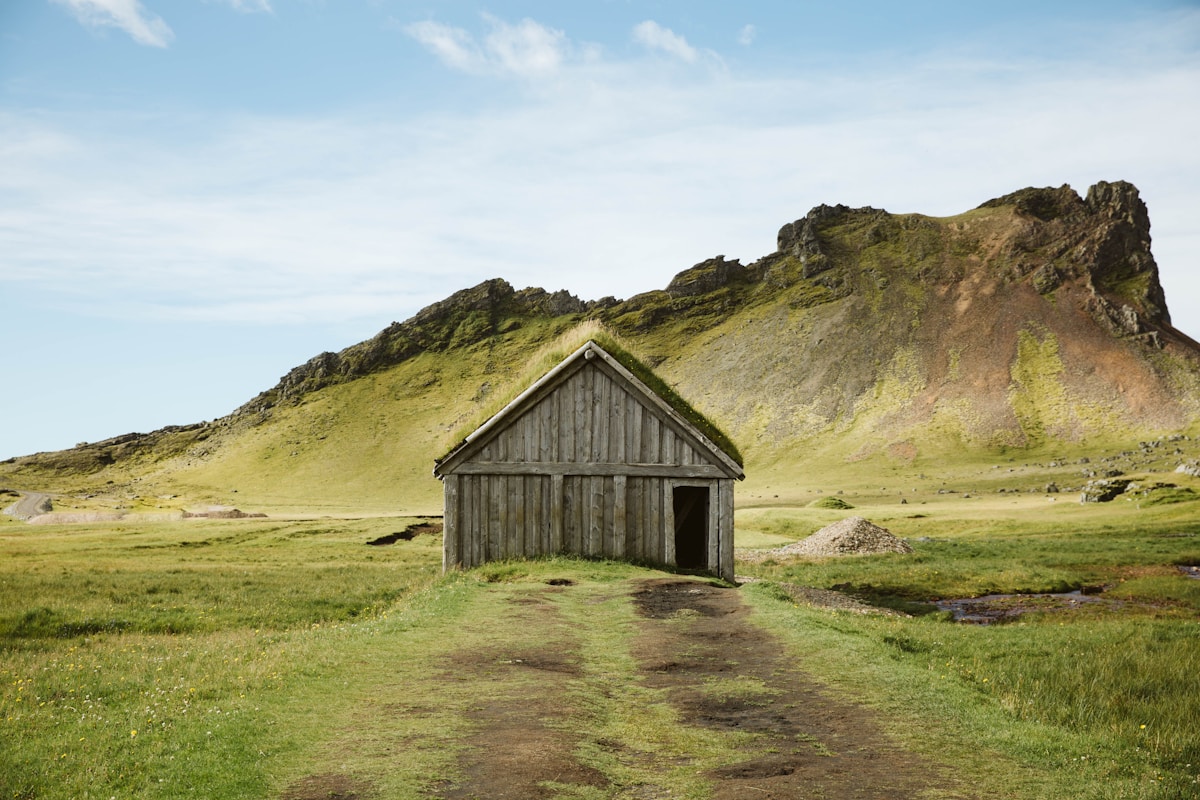 Brown wooden farmhouse on a green grass field near mountains, Iceland countryside