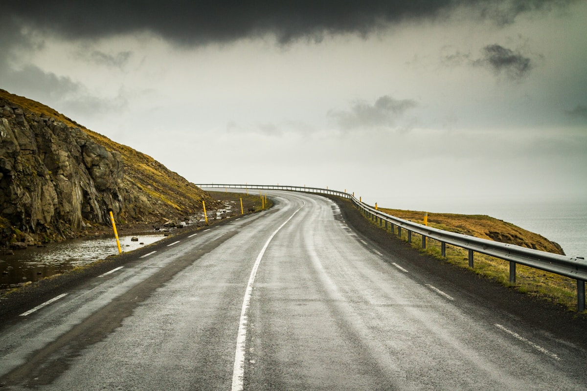 Grey asphalt road stretching through brown grass field under a cloudy sky, Snæfellsnes, Iceland