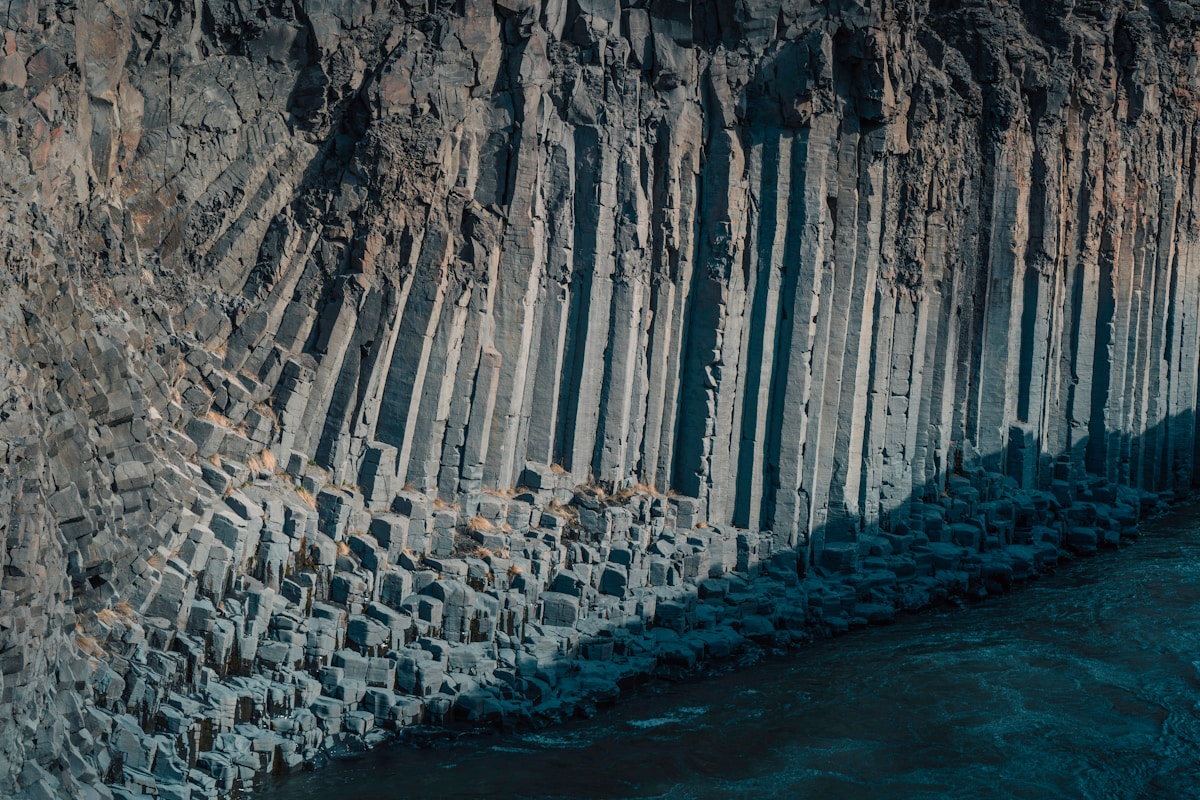 Turquoise river flowing between tall hexagonal basalt columns in Studlagil Canyon, East Iceland