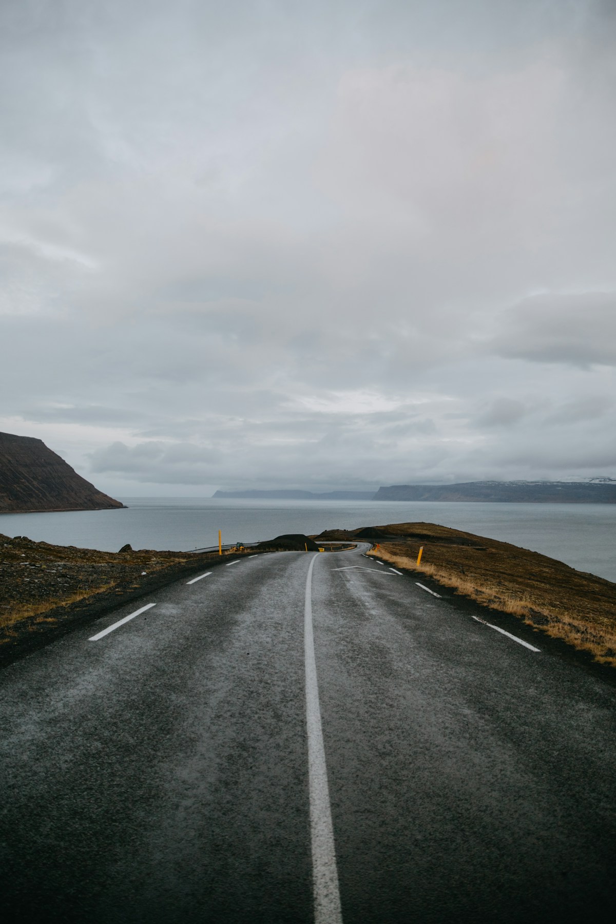 Grey asphalt road going on the body of water toward dramatic Westfjords mountains, Súðavík, Iceland