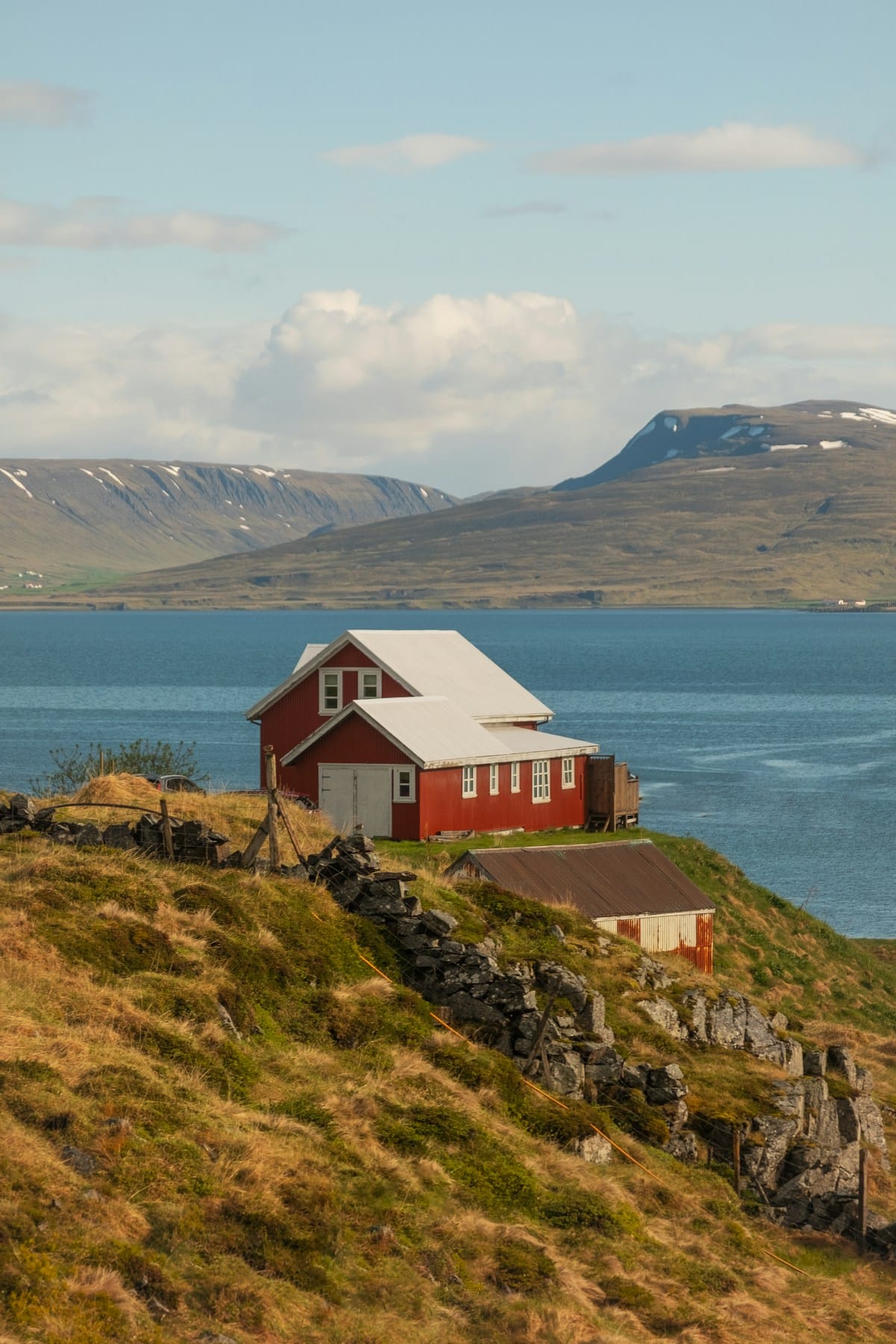Red farmhouse on a hillside above an Icelandic fjord with mountains behind