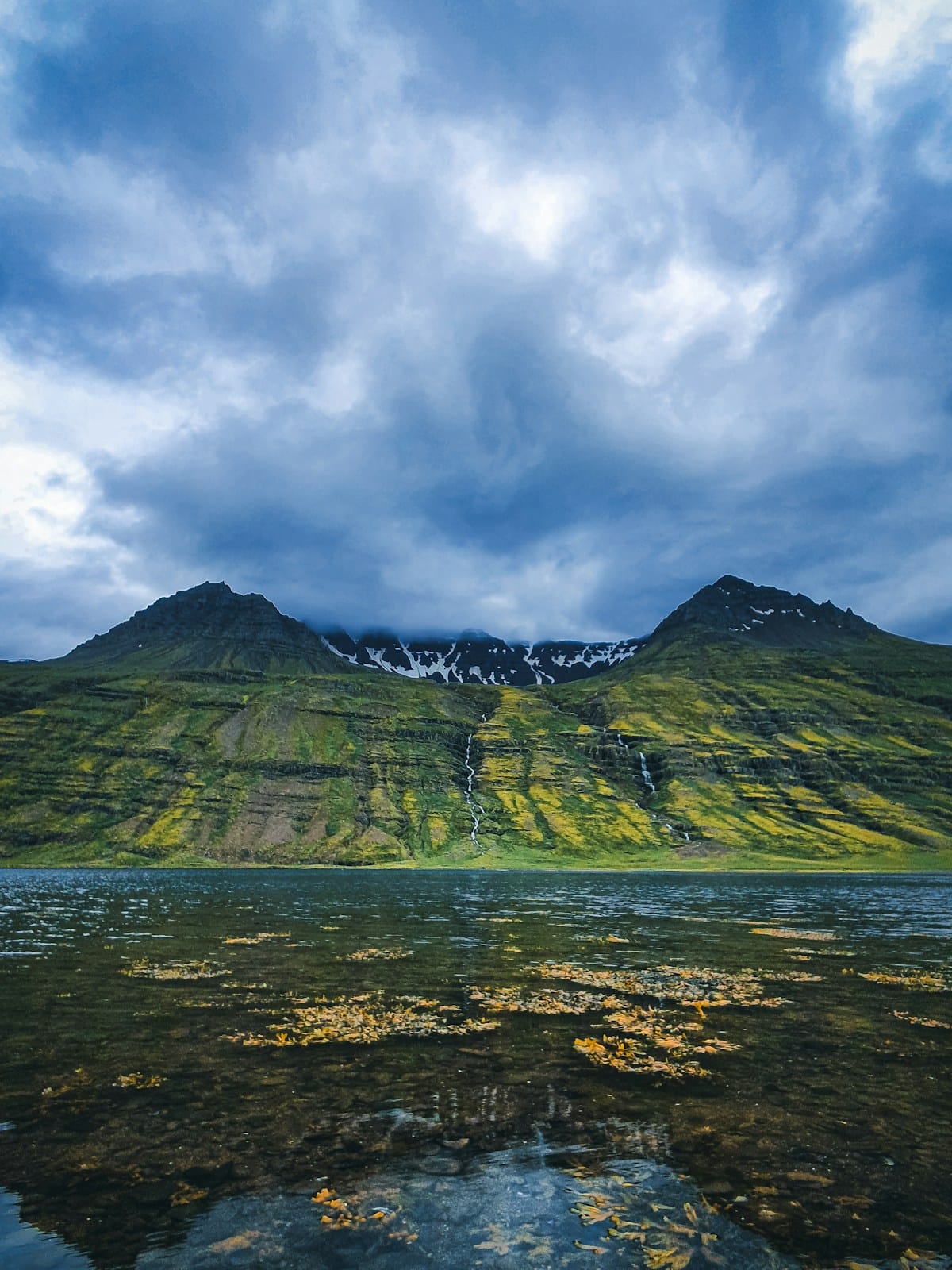 Green fjord mountain with waterfalls reflected in calm water, east Iceland