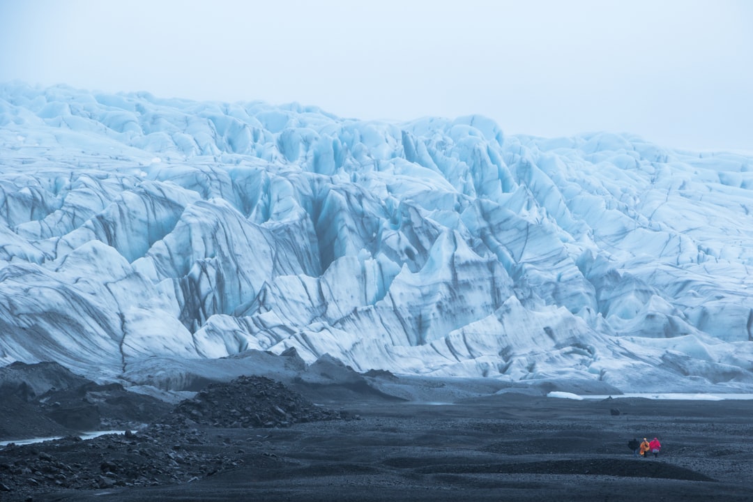 Vatnajökull glacier face with tiny hikers on black sand below
