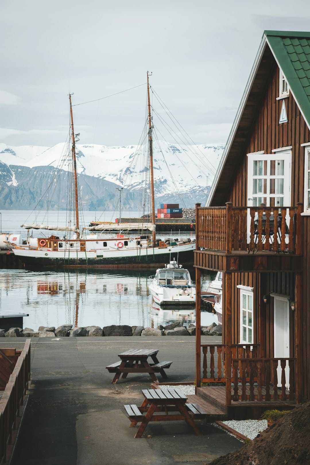 Húsavík harbour with wooden guesthouse, sailboat, and snow-capped mountains