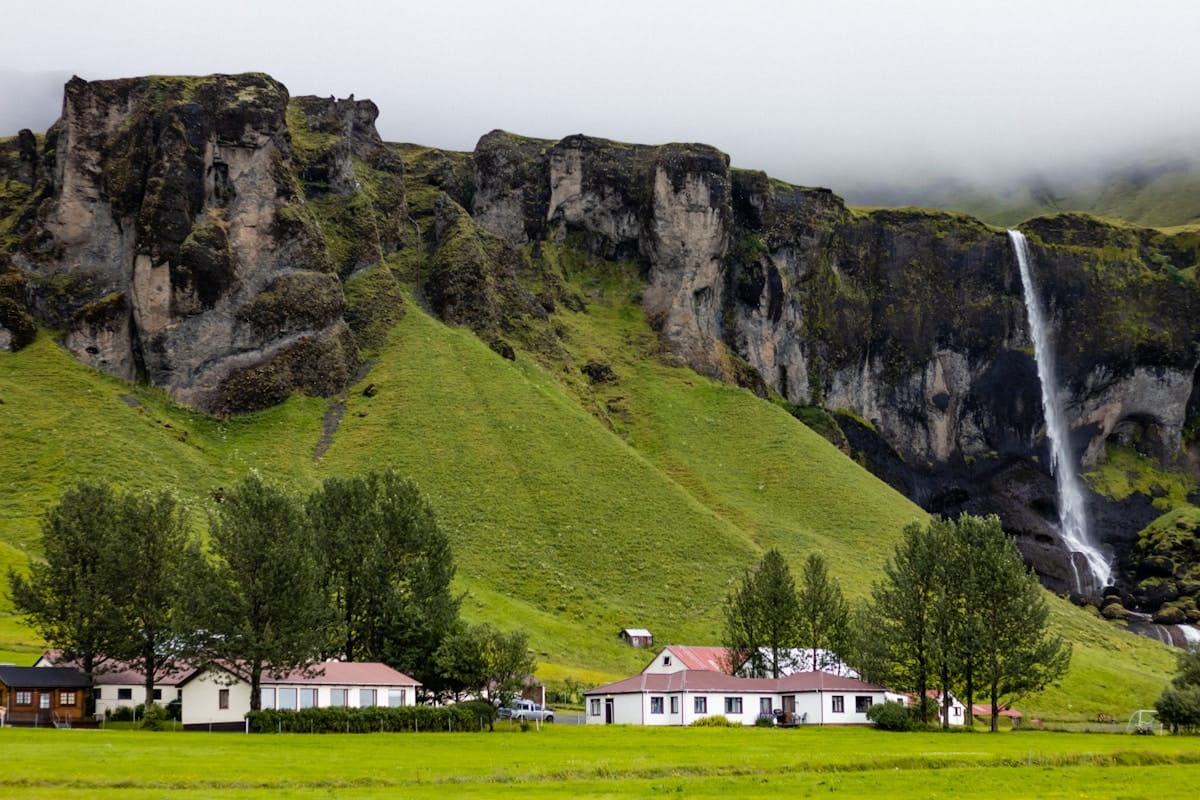 White houses at the base of lush green cliffs with a waterfall, north Iceland