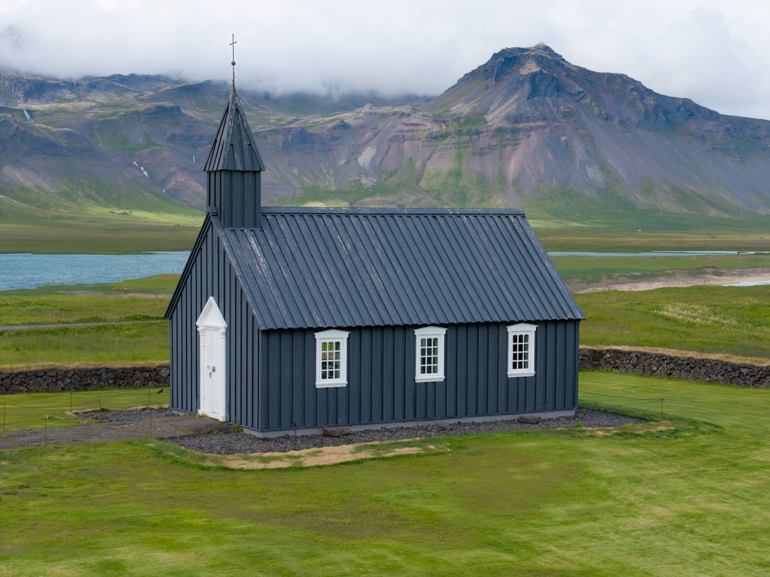 Búðakirkja black church on green lava field, Snæfellsnes mountains in cloud behind