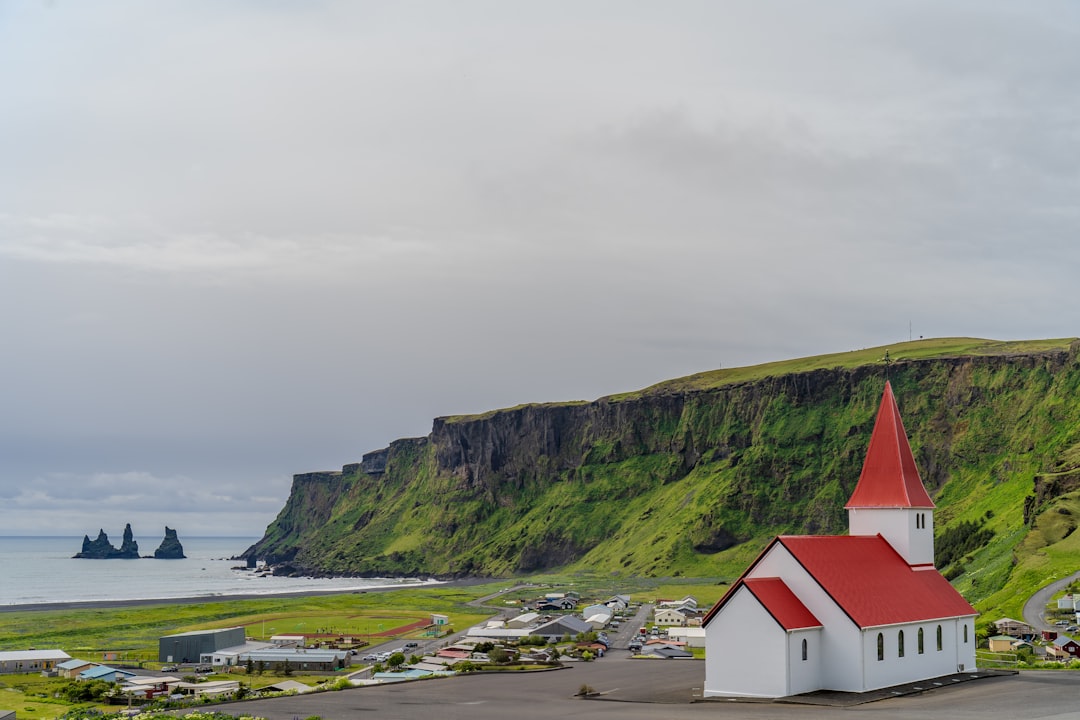 Vík church with red roof above the village, Reynisfjara cliffs and sea stacks behind